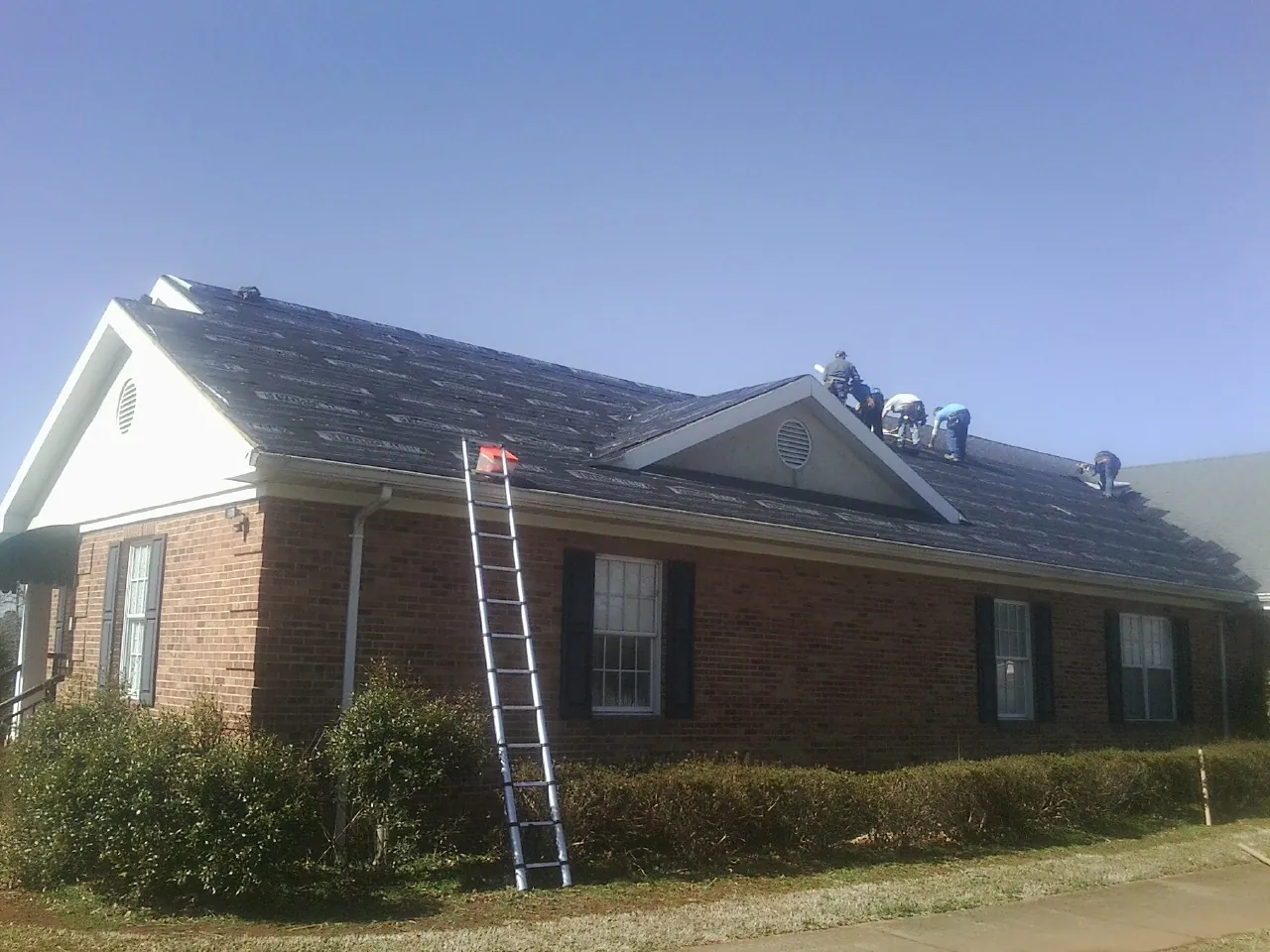 Crew tearing shingles off a brick ranch roof with a ladder set — Metal Roof Repair work by our crew in South Dennis