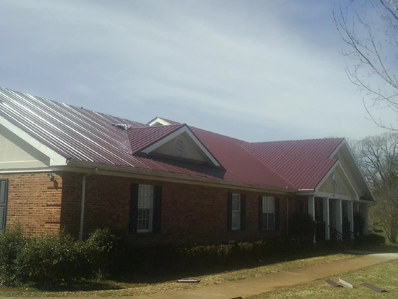 Red metal roof with gabled entries on a long brick building, from a Hail Damage Roof Repair job in South Dennis