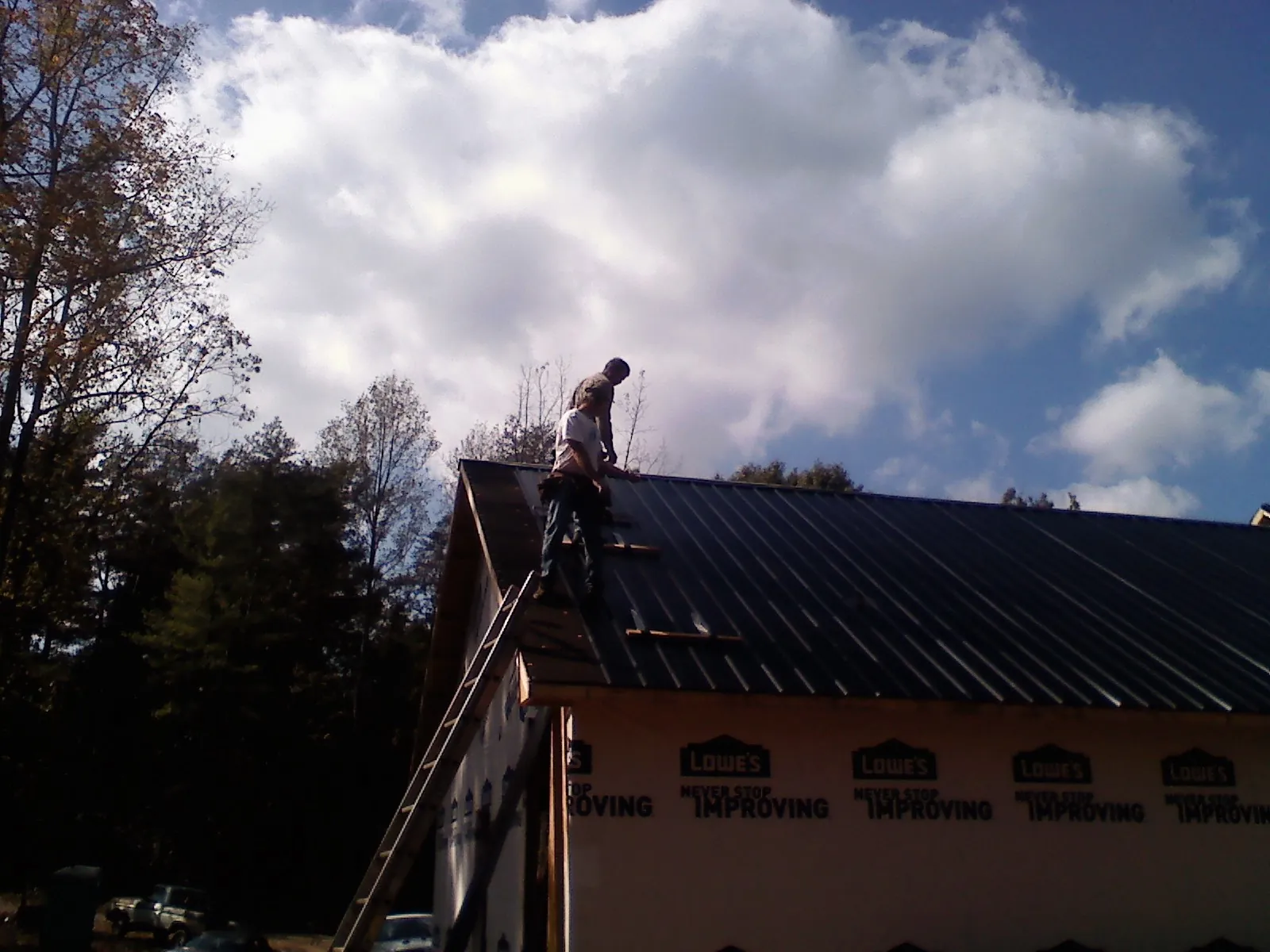 Roofer fastening dark metal panels high against a cloudy sky, from a Roof Inspection job in South Dennis