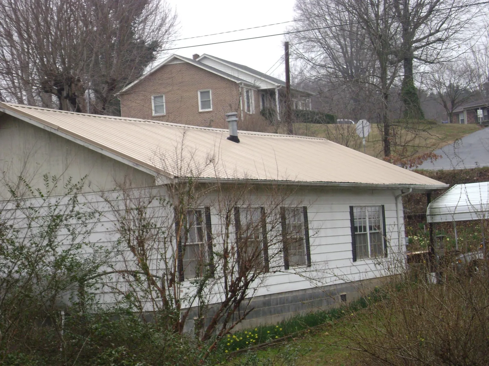 Tan metal roof on a white sided house set into a hillside — Commercial Roofing by Roofing Brothers in South Dennis